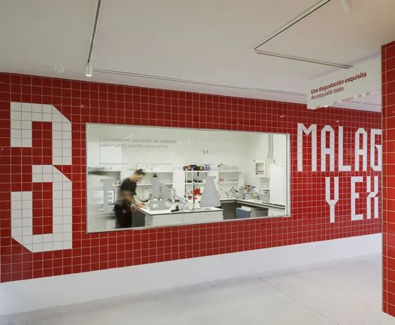 Interior de la Fábrica Cervezas Victoria mostrando una pared de azulejos rojos con gran tipografía blanca y una ventana hacia el área de cocina donde una persona está trabajando