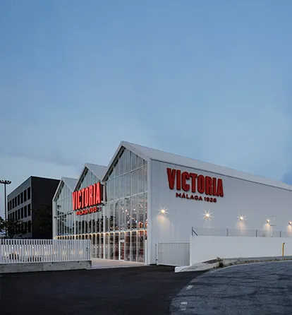 Fachada blanca de la fábrica de cerveza con letras grandes rojas 'VICTORIA MÁLAGA 1928' al atardecer