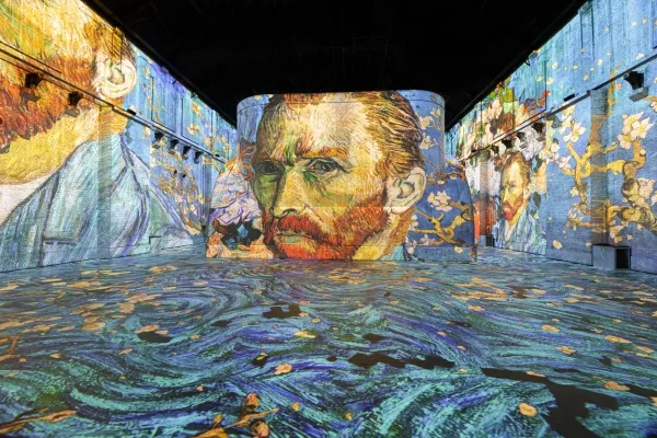 Proyección digital inmersiva del retrato de Vincent van Gogh y patrones arremolinados en pantallas cilíndricas y suelo dentro de una habitación oscura.