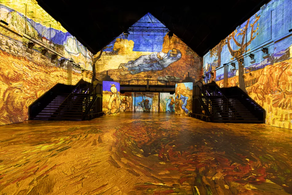 Sala de exposición digital inmersiva con pinturas al estilo Van Gogh proyectadas en paredes, suelo y techo, con una escalera central e iluminación ambiental