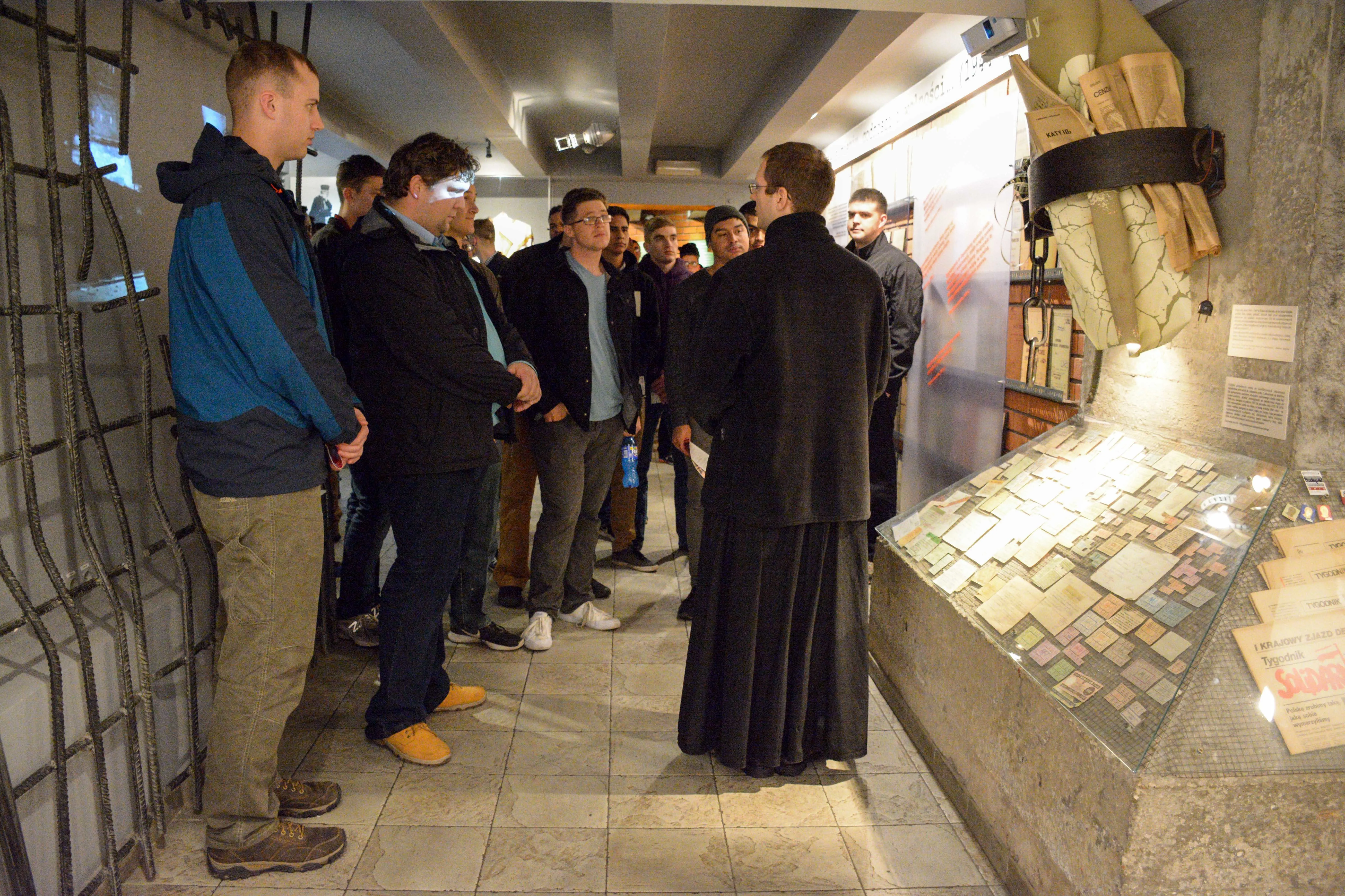 Grupo de personas, incluyendo un sacerdote, observando una vitrina con documentos y artefactos en una galería de museo.