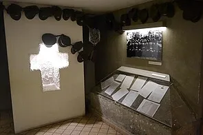 Vitrine met documenten en een foto, kruisvormig licht en kappen aan de muur