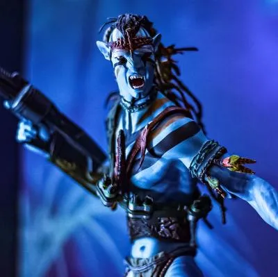 Una figura de acción detallada de un guerrero Na'vi de Avatar, con piel azul, rastas y armadura tribal, sosteniendo un arma