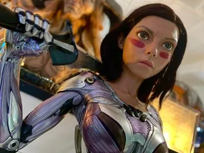 Primer plano de una figura a tamaño real con un traje futurista con armadura de color púrpura metálico y plateado y un brazo robótico