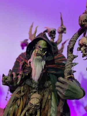 personaje de fantasía de piel verde con barba blanca larga, vistiendo capa con capucha y sosteniendo un bastón