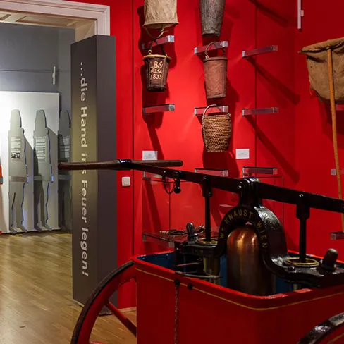 zabytkowa pompa strażacka i zabytkowy sprzęt strażacki na wystawie w muzeum z czerwonymi ścianami