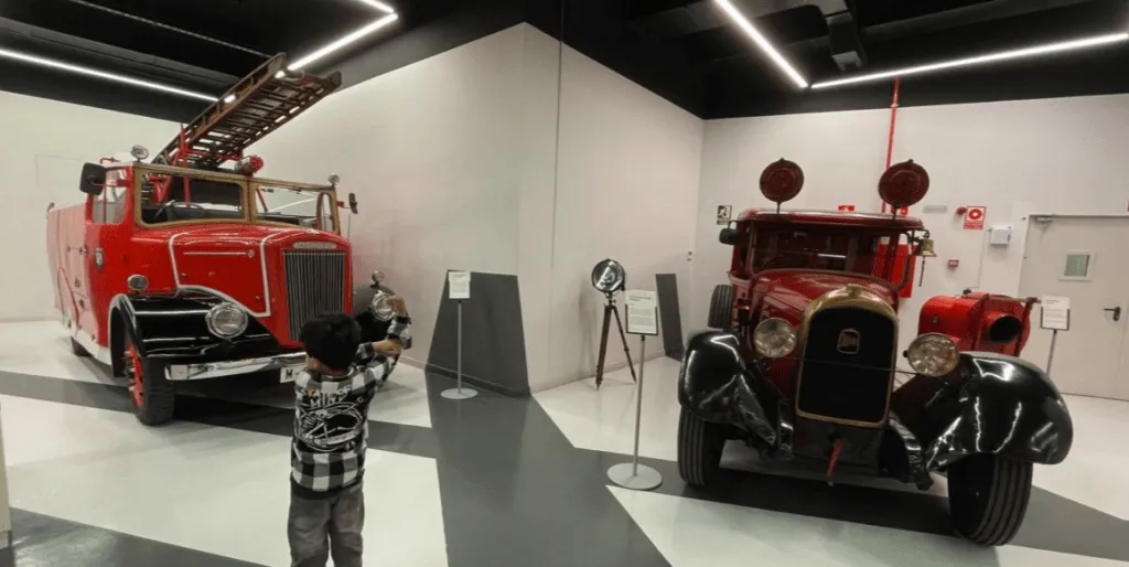 Dos camiones de bomberos antiguos rojos en exhibición en un museo con un niño delante