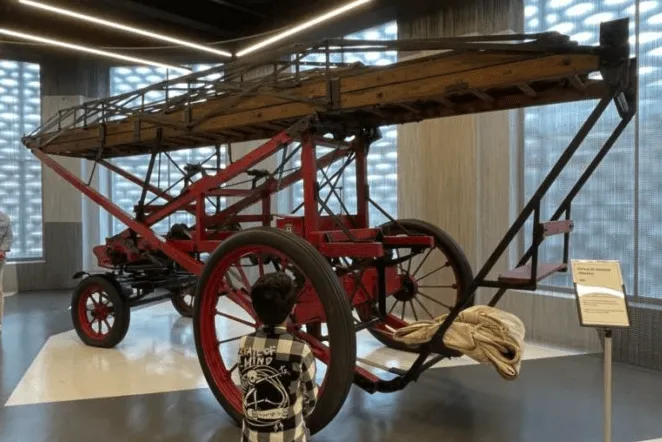 Un camión de bomberos de escalera vintage rojo con ruedas grandes en exhibición en una galería de museo.