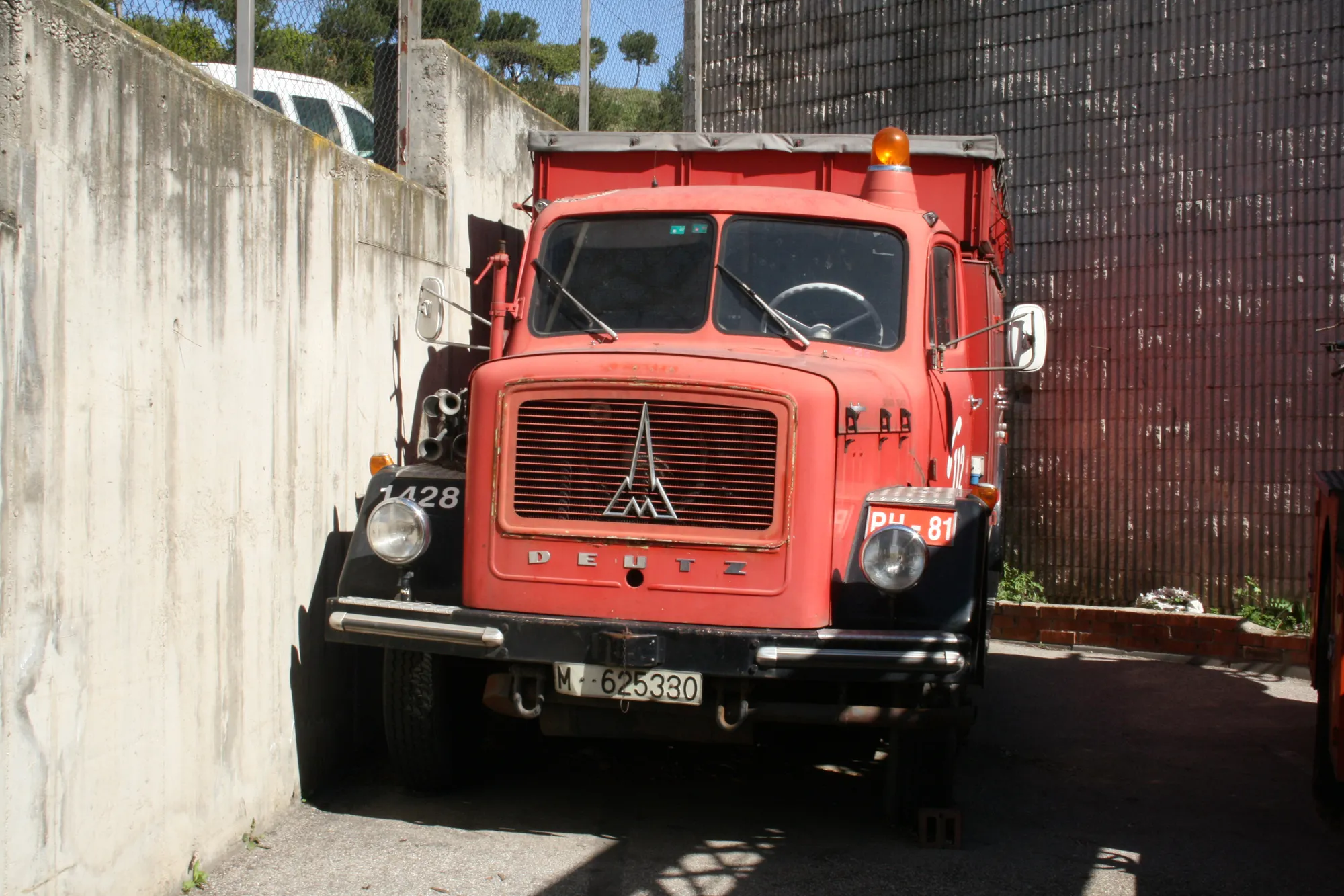Camión de bomberos vintage rojo con una parrilla y faros prominentes, estacionado junto a una pared de hormigón