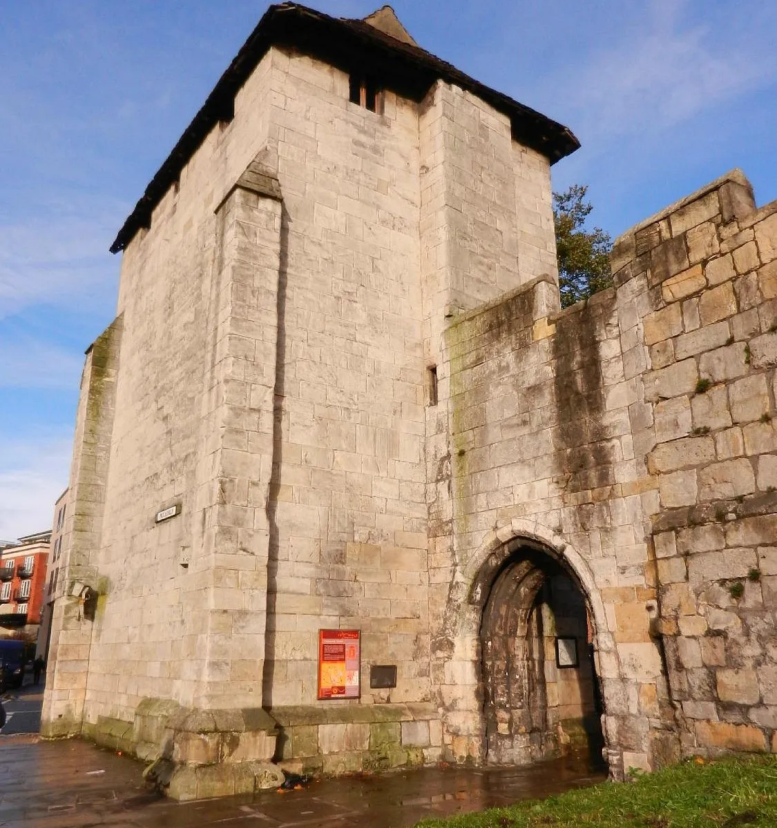 Torre de piedra medieval con entrada de madera arqueada adosada a las murallas de la ciudad de York bajo un cielo azul