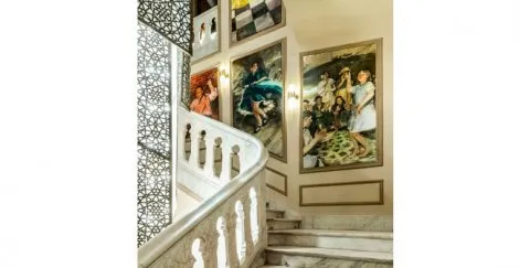 Una gran escalera con balaustradas blancas, obras de arte enmarcadas en las paredes y una pantalla geométrica decorativa.