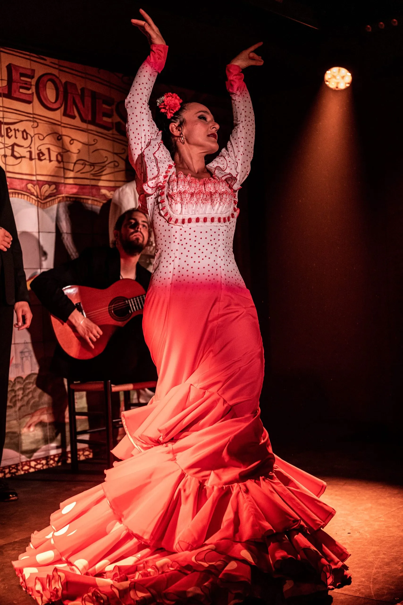 Bailaora de flamenco con un vestido de lunares rojos y blancos actuando en el escenario con un guitarrista detrás de ella