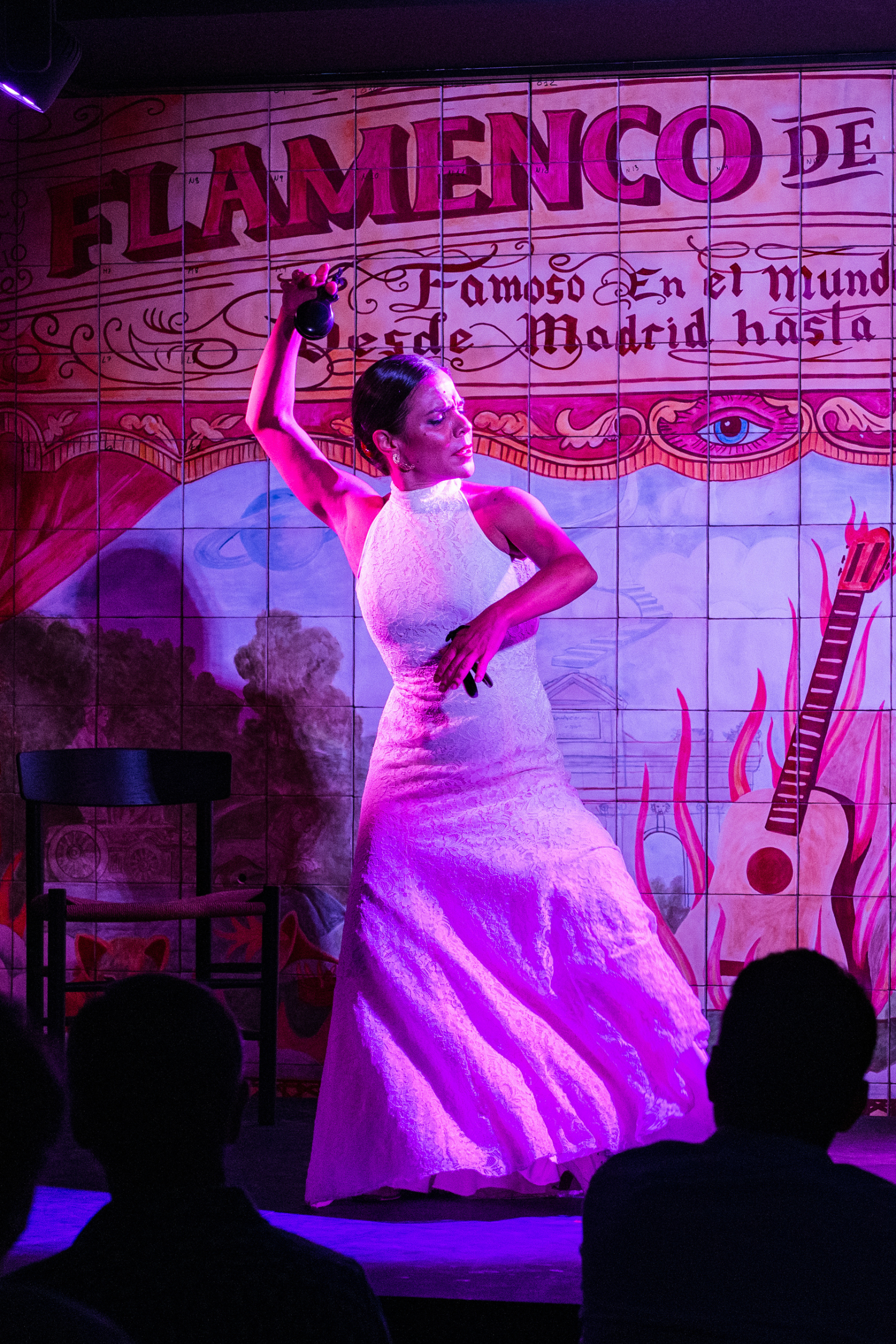 Una mujer con un vestido blanco baila en el escenario bajo luces púrpuras con un telón de fondo que dice 'Flamenco de Leones' y 'Famoso En el Mundo Desde Madrid hasta'