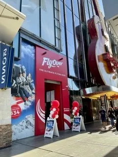 Fachada de entrada roja con el logotipo y la marca de FlyOver bajo una gran escultura de guitarra en una calle de Las Vegas