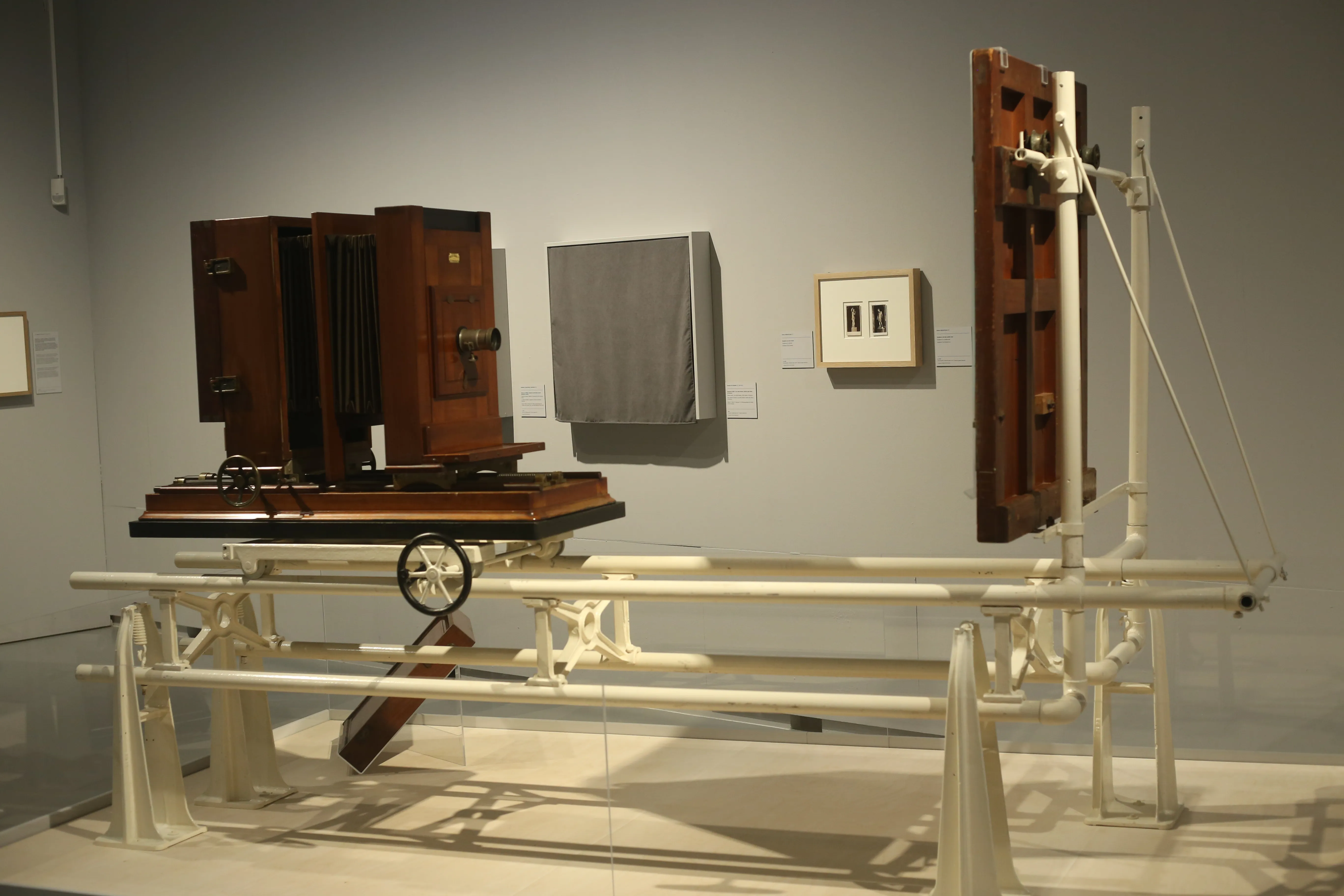 Gran cámara antigua de madera montada sobre un sistema de rieles de metal blanco expuesta en una sala de museo con paredes grises