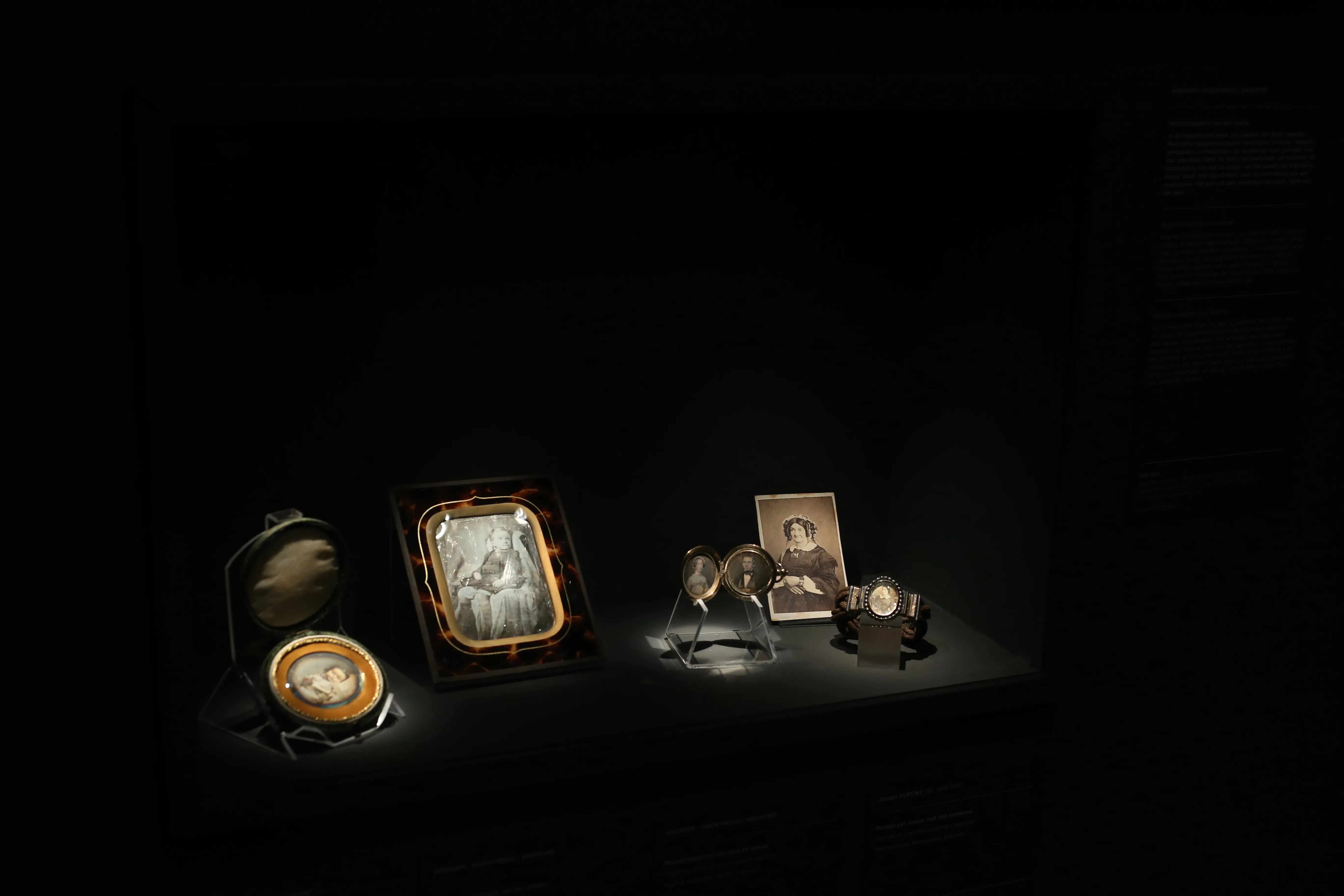 Retratos fotográficos antiguos enmarcados y miniaturas de retratos dispuestos sobre una superficie bajo focos, sobre un fondo oscuro en una exposición de museo