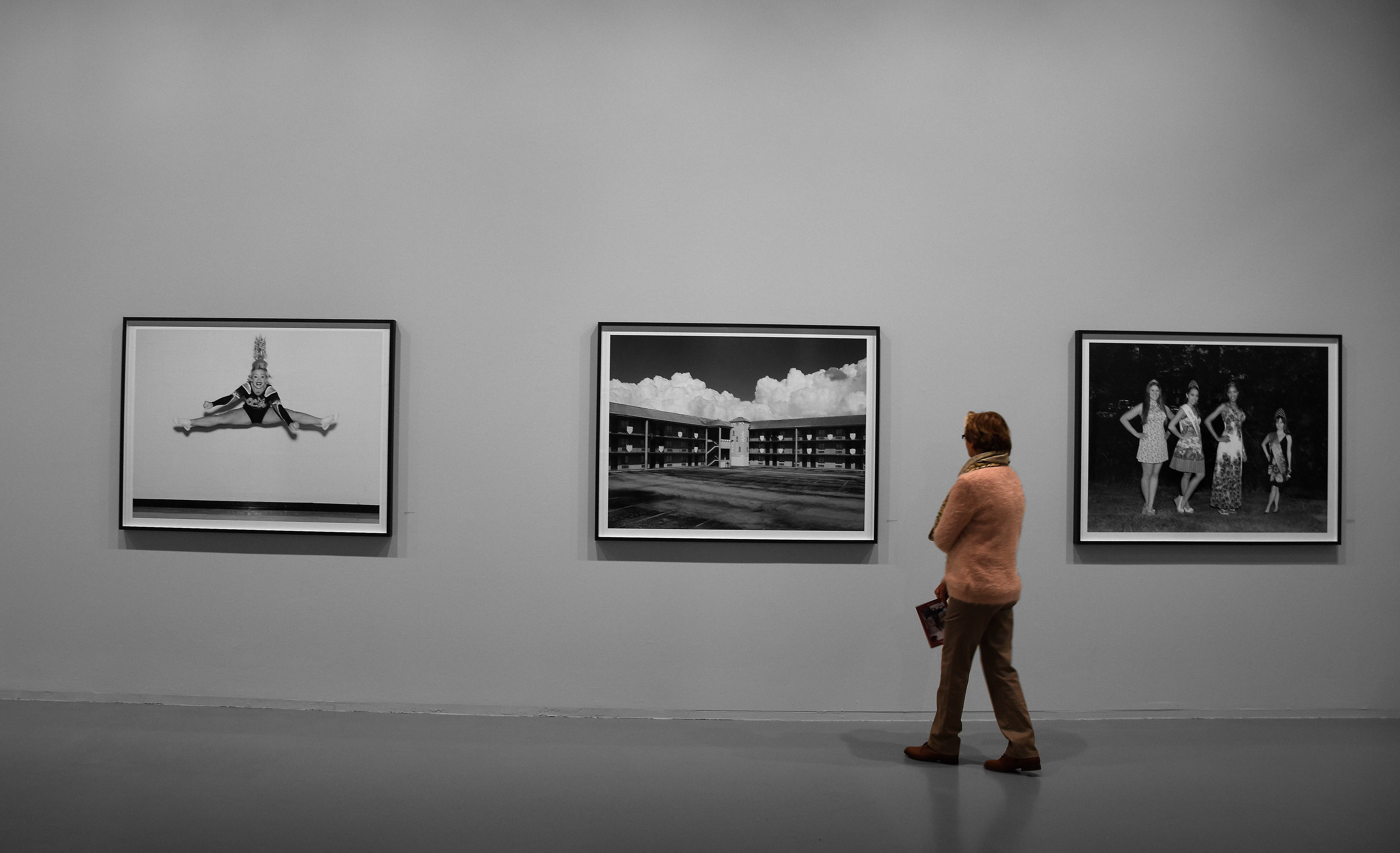 Un visitante está de pie en una galería observando tres fotografías en blanco y negro enmarcadas que cuelgan de una pared gris.