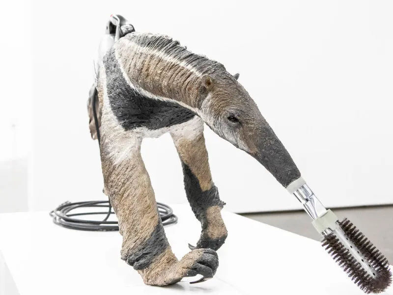 Escultura de un oso hormiguero gigante con un cepillo de pelo sujeto al hocico, con un cable enrollado en el suelo