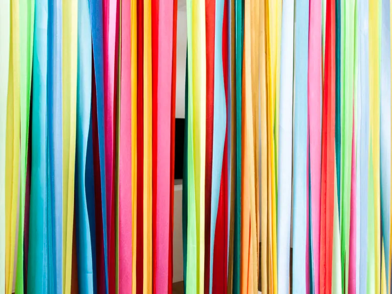 Tiras verticales de tela de colores en amarillo, azul, verde, rosa, rojo y naranja que cuelgan una al lado de la otra como instalación artística
