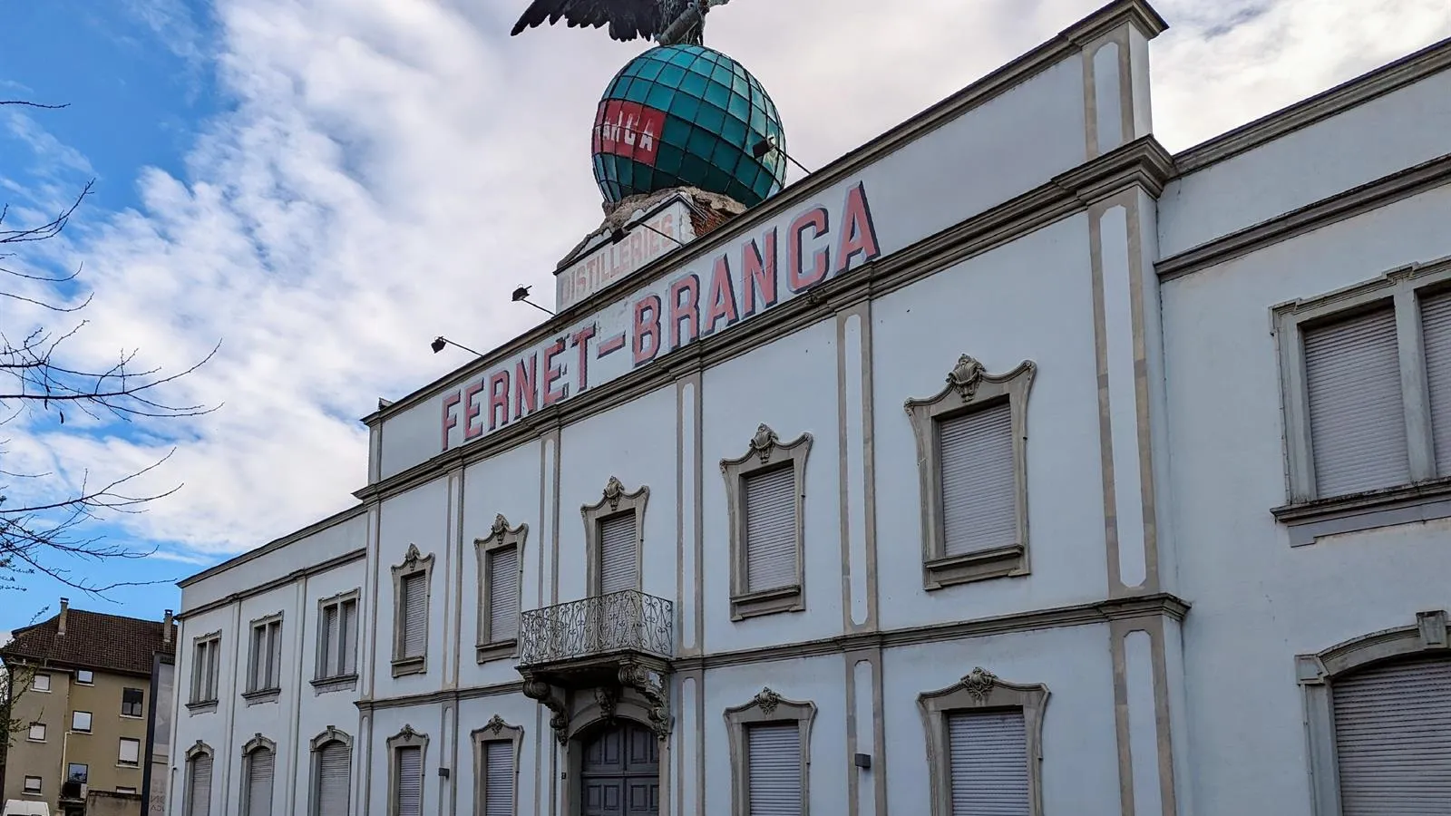 Biała fasada z napisem FERNET-BRANCA oraz zielony glob zwieńczony rzeźbą orła