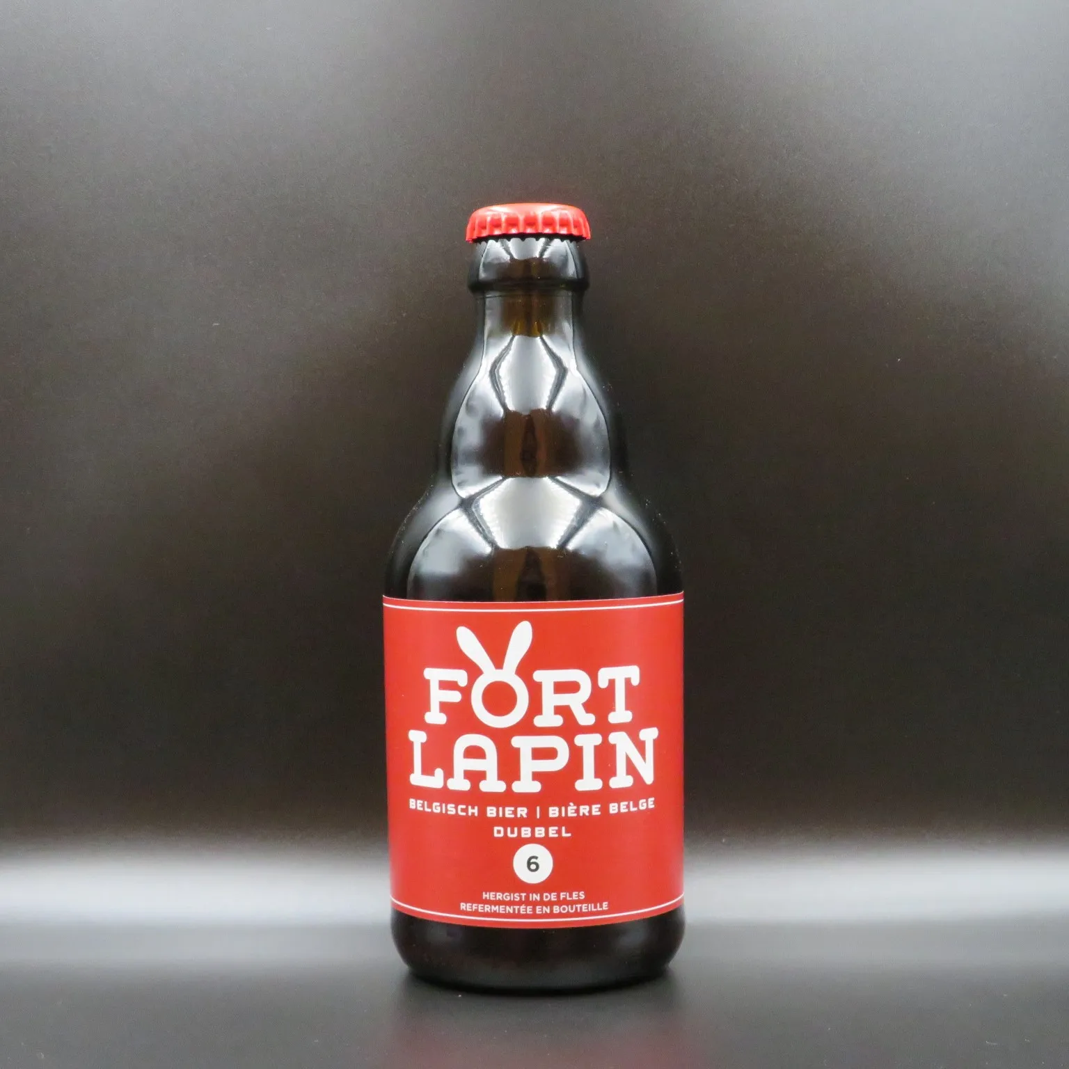 Botella de cerveza de cristal marrón con una etiqueta roja que presenta el texto blanco 'FORT LAPIN DUBBEL' y un logotipo de un conejo, coronada con una chapa roja sobre un fondo oscuro.