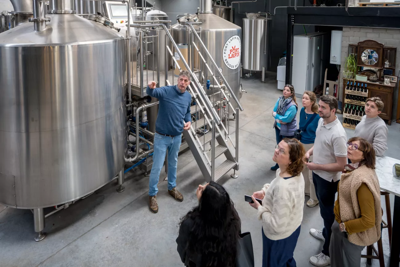 Un guía señala unos grandes tanques de fermentación de acero inoxidable mientras un pequeño grupo de turistas escucha en la zona de producción de la cervecería Fort Lapin.