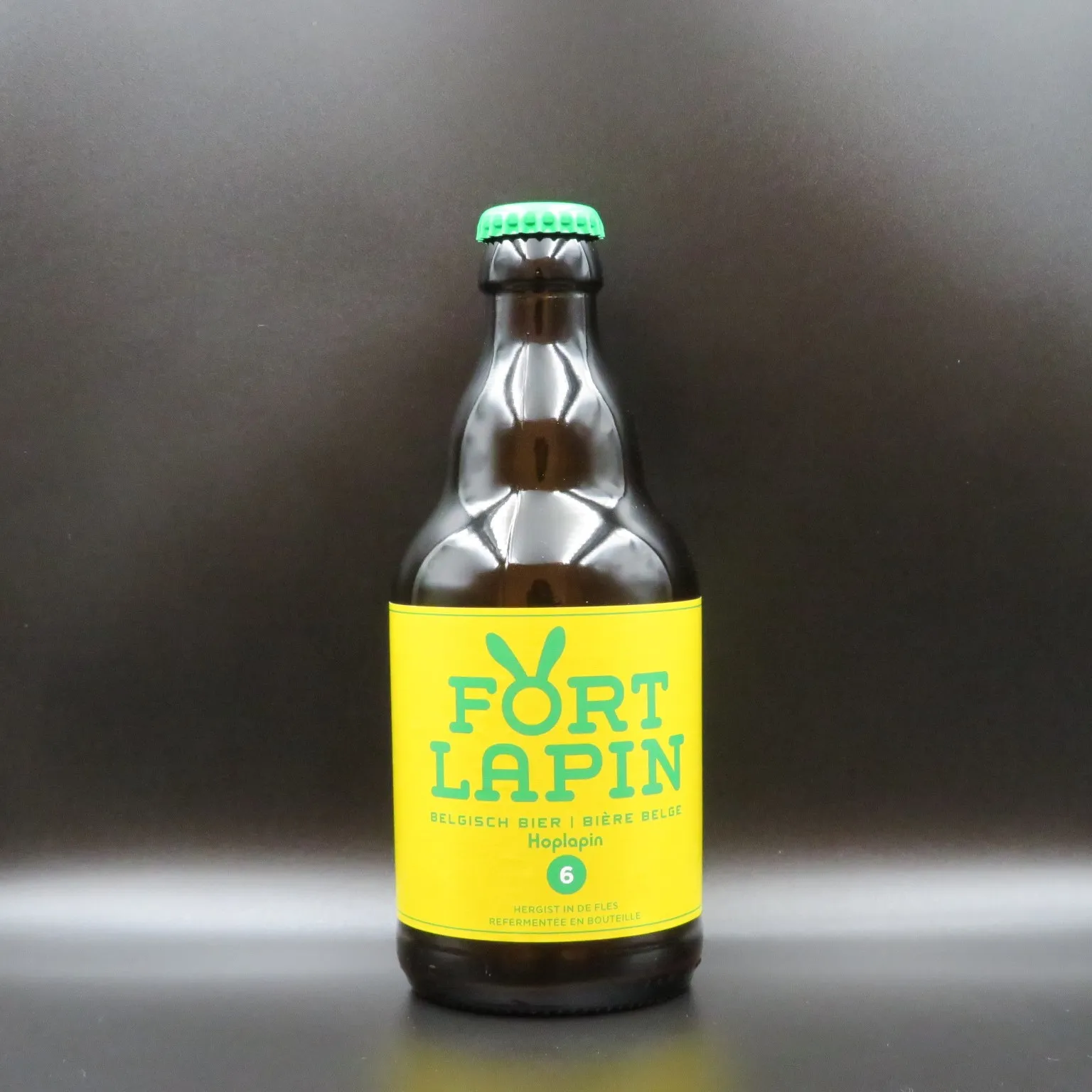 Una botella de cerveza de cristal marrón con una etiqueta de color amarillo brillante que dice 'FORT LAPIN' y una chapa verde, sobre un fondo gris oscuro.