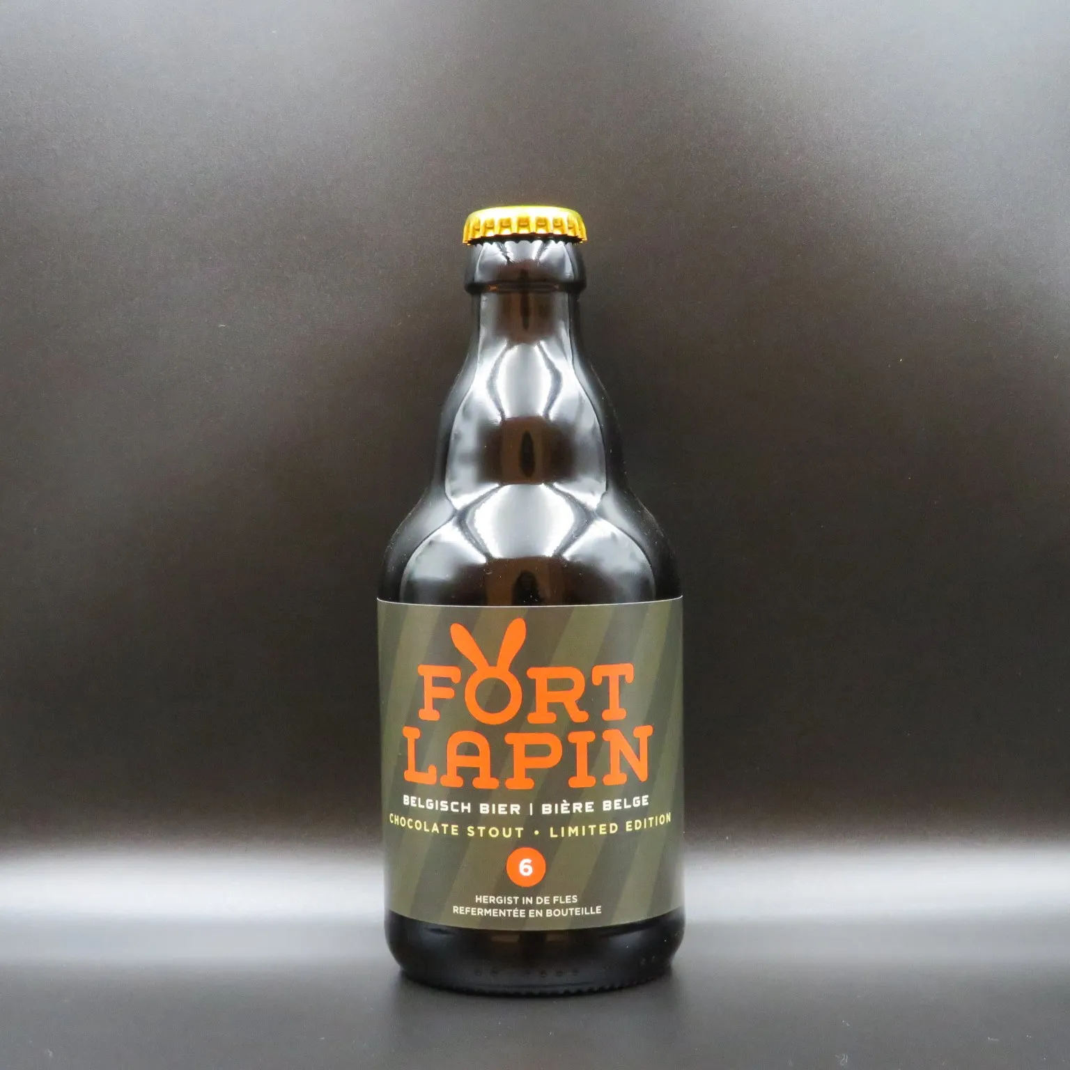 Brązowa szklana butelka belgijskiego piwa Fort Lapin z oliwkowozieloną etykietą z pomarańczowym napisem 'Fort Lapin' i 'Chocolate Stout Limited Edition', zakończona żółtym kapslem, na ciemnoszarym tle