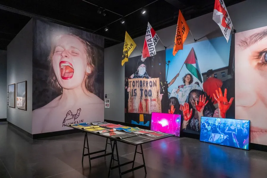 Fototentoonstelling met grote afdrukken, protestvlaggen en digitale displays in een galerie