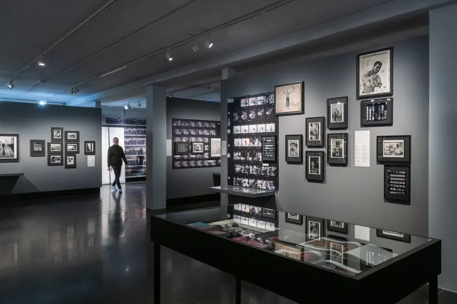 Galerij met ingelijste foto's aan grijze muren en een glazen vitrine op de voorgrond