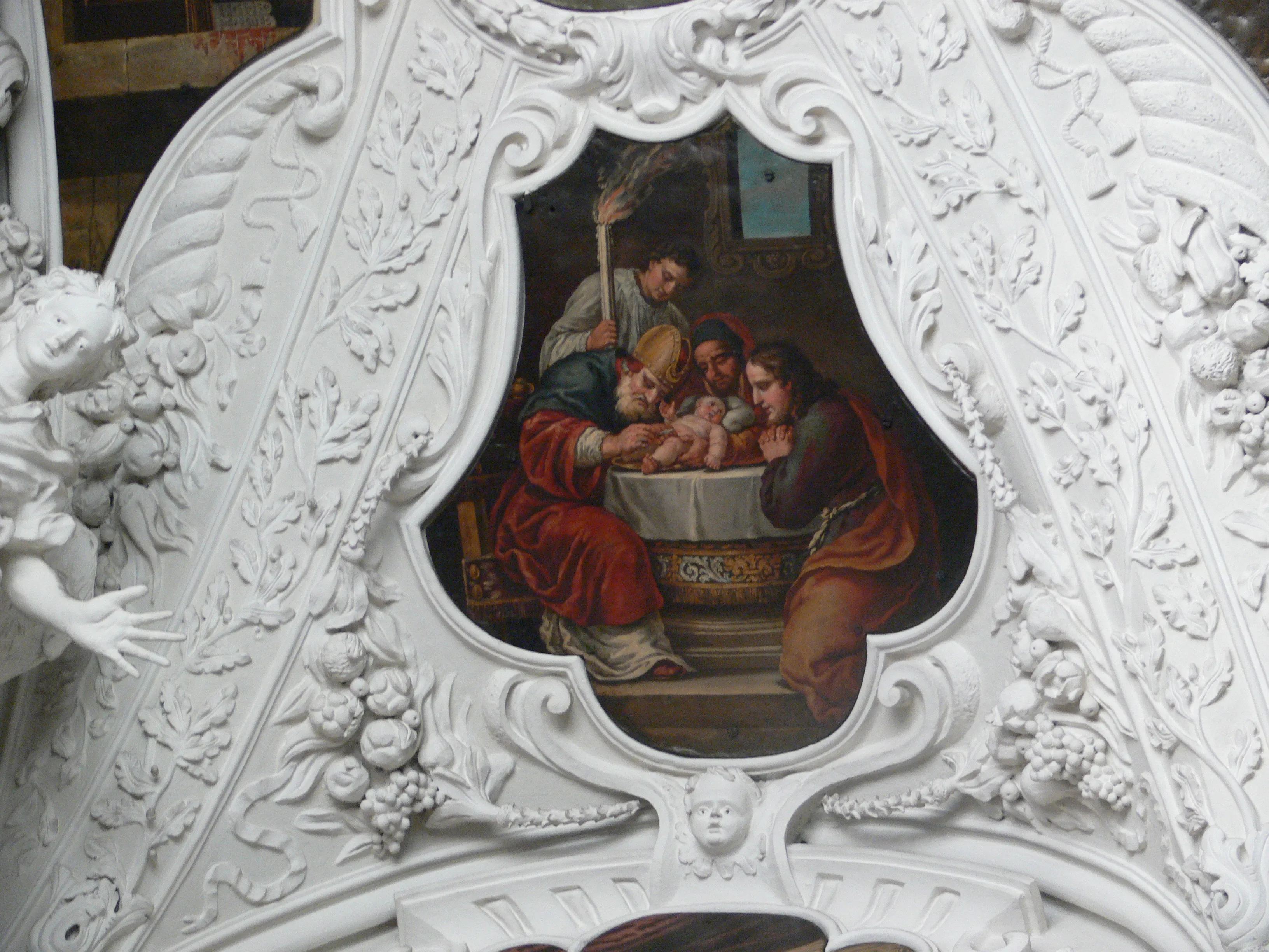 Close-up van een sierlijke witte barokke stucwerklijst rondom een religieus schilderij dat figuren voorstelt die zich rond een centraal bekken hebben verzameld.