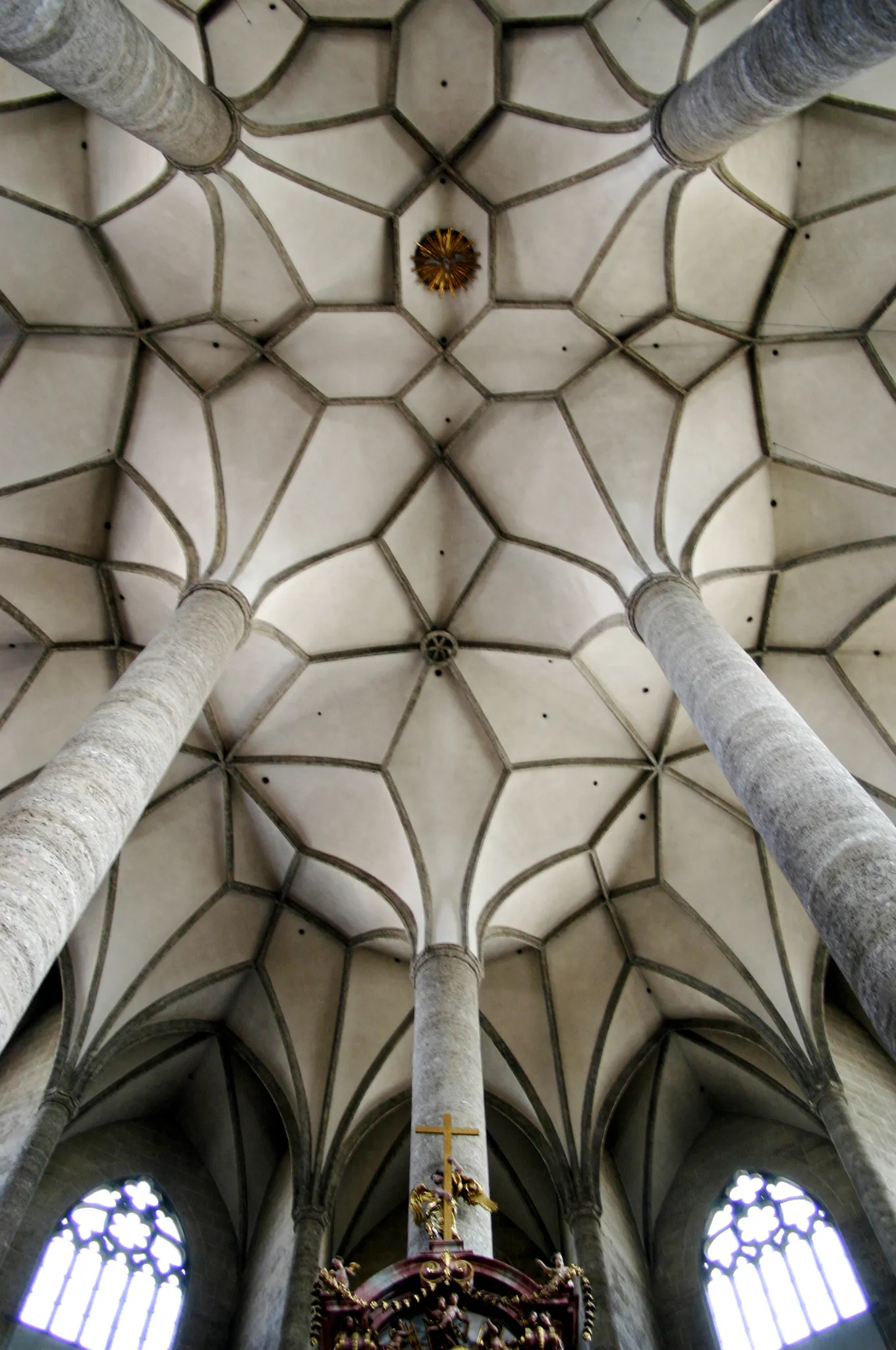 Upward view of the intricate ribbed vault ceiling with stone columns and a golden crucifix above a baroque altar inside the Franciscan Church Salzburg