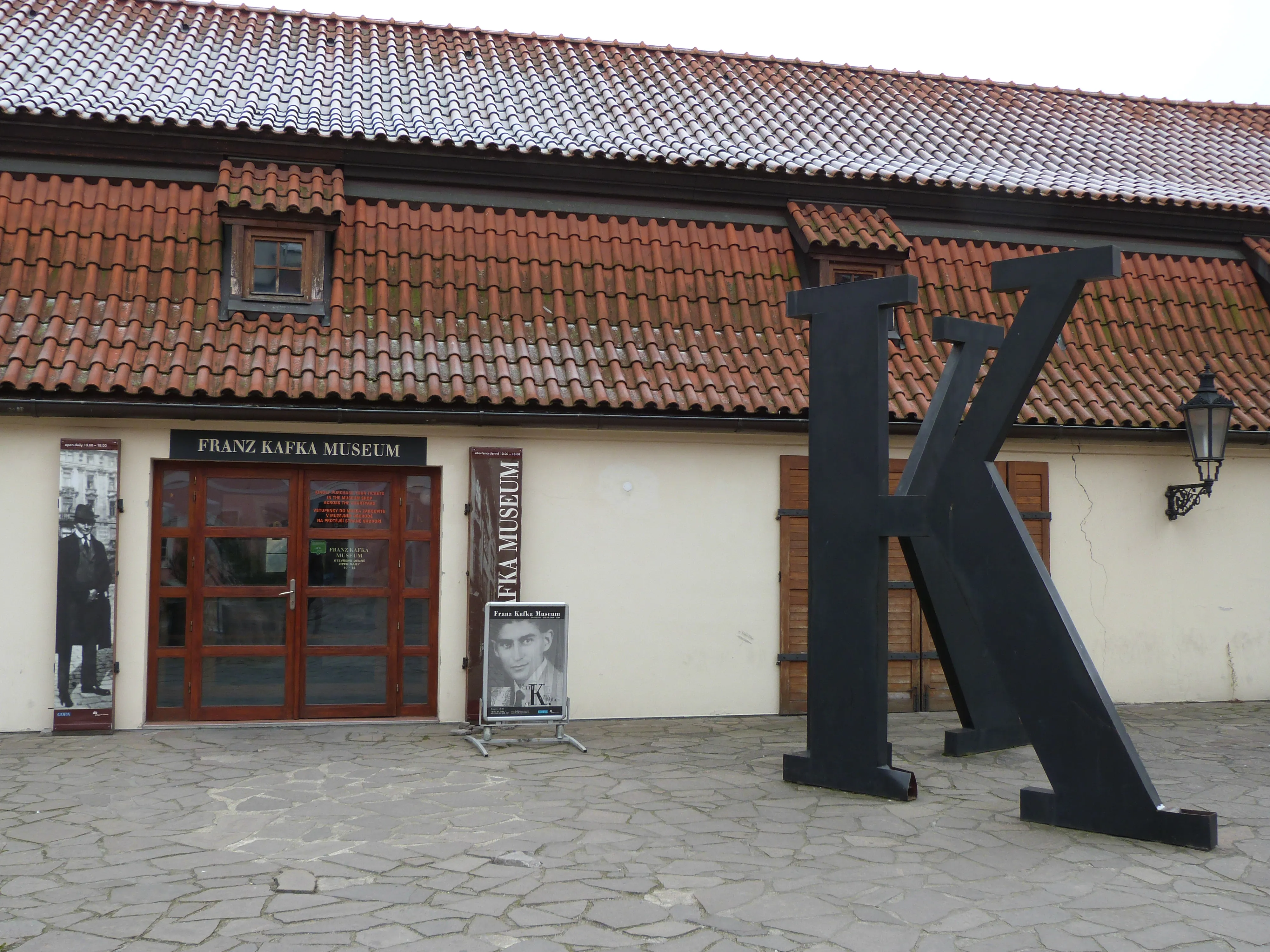 De ingang van het Franz Kafka Museum met een groot zwart 'K'-beeld en een bord boven de deuren