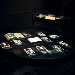 Ronde donkere tafel met verlichte panelen die foto's en documenten tonen in een schemerige tentoonstellingsruimte