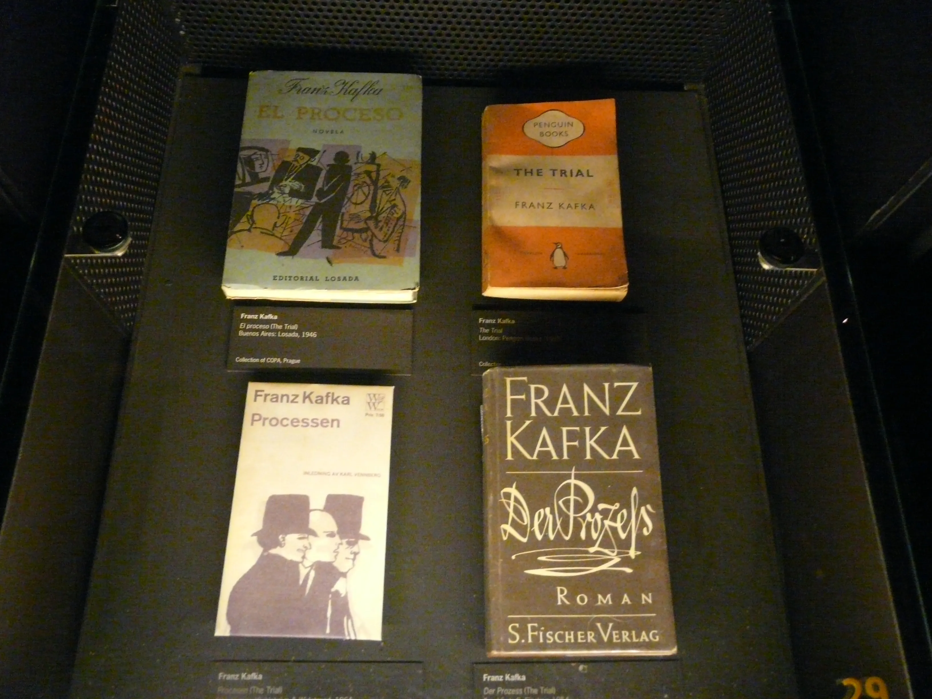 Tentoonstelling met boeken van Franz Kafka, waaronder 'De Gedaanteverwisseling', 'Het Proces', 'De Maledicten' en 'Het Slot', in een vitrine