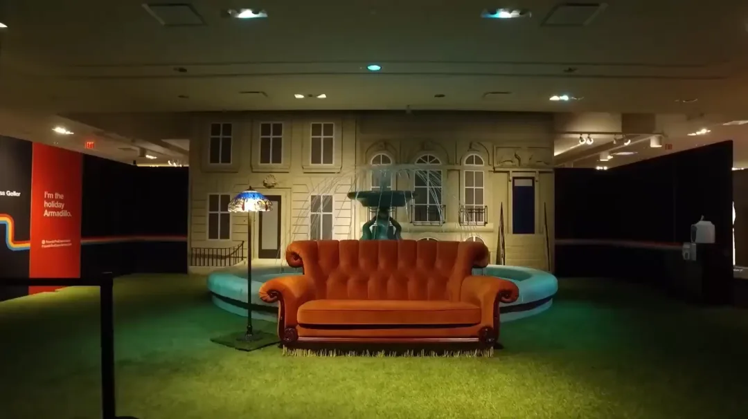 Orange sofa in a recreated Central Perk set with a building facade and green carpet