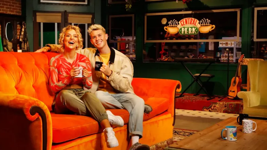 Two people sitting on the orange couch from the FRIENDS™ TV show, with a Central Perk sign in the background