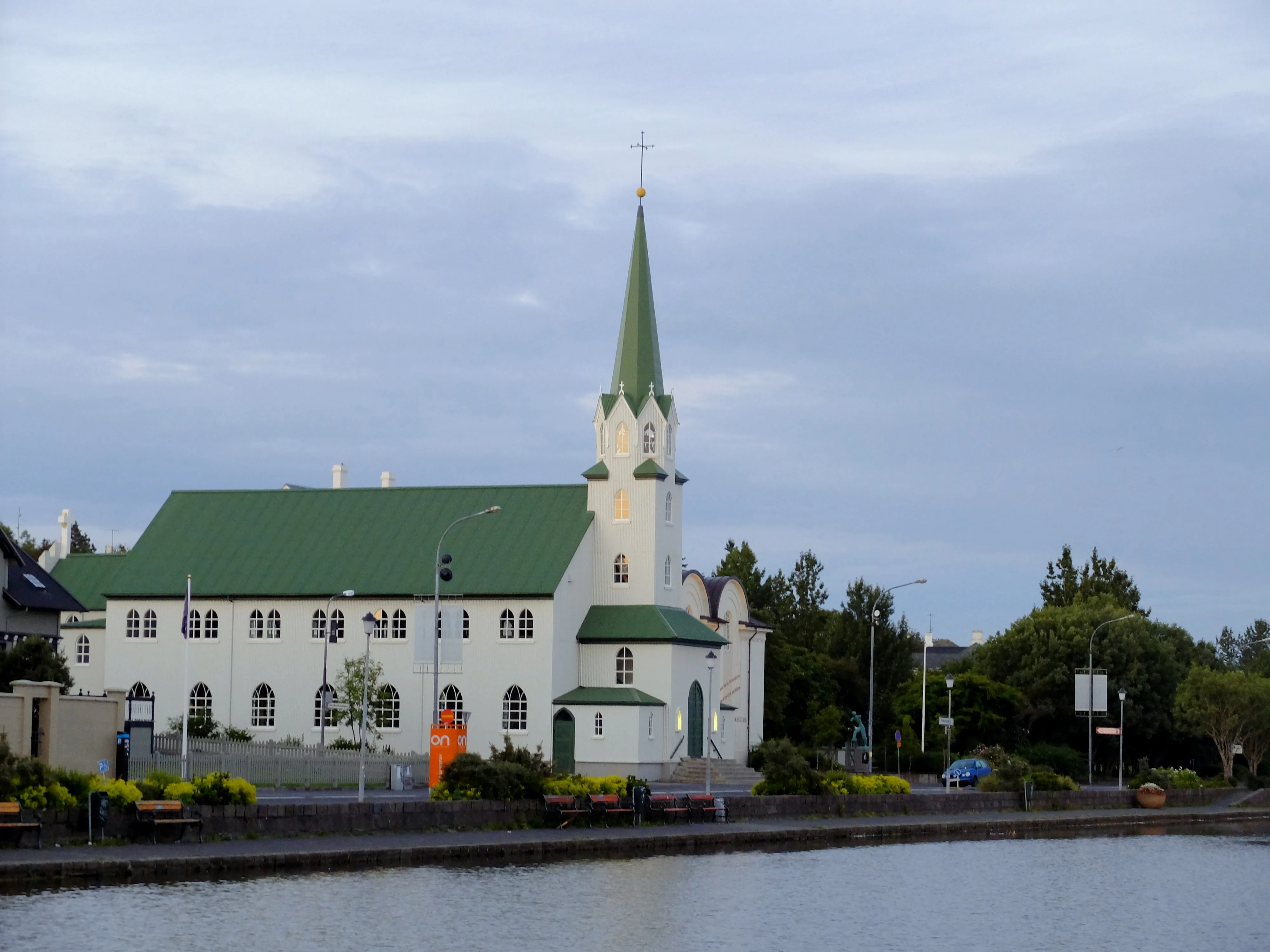 Iglesia blanca con techo verde y una alta torre verde con vistas al agua, Fríkirkjan í Reykjavík