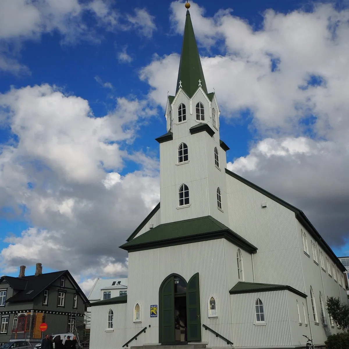 Iglesia de madera blanca con un alto campanario verde y tejado verde sobre un cielo azul con nubes blancas