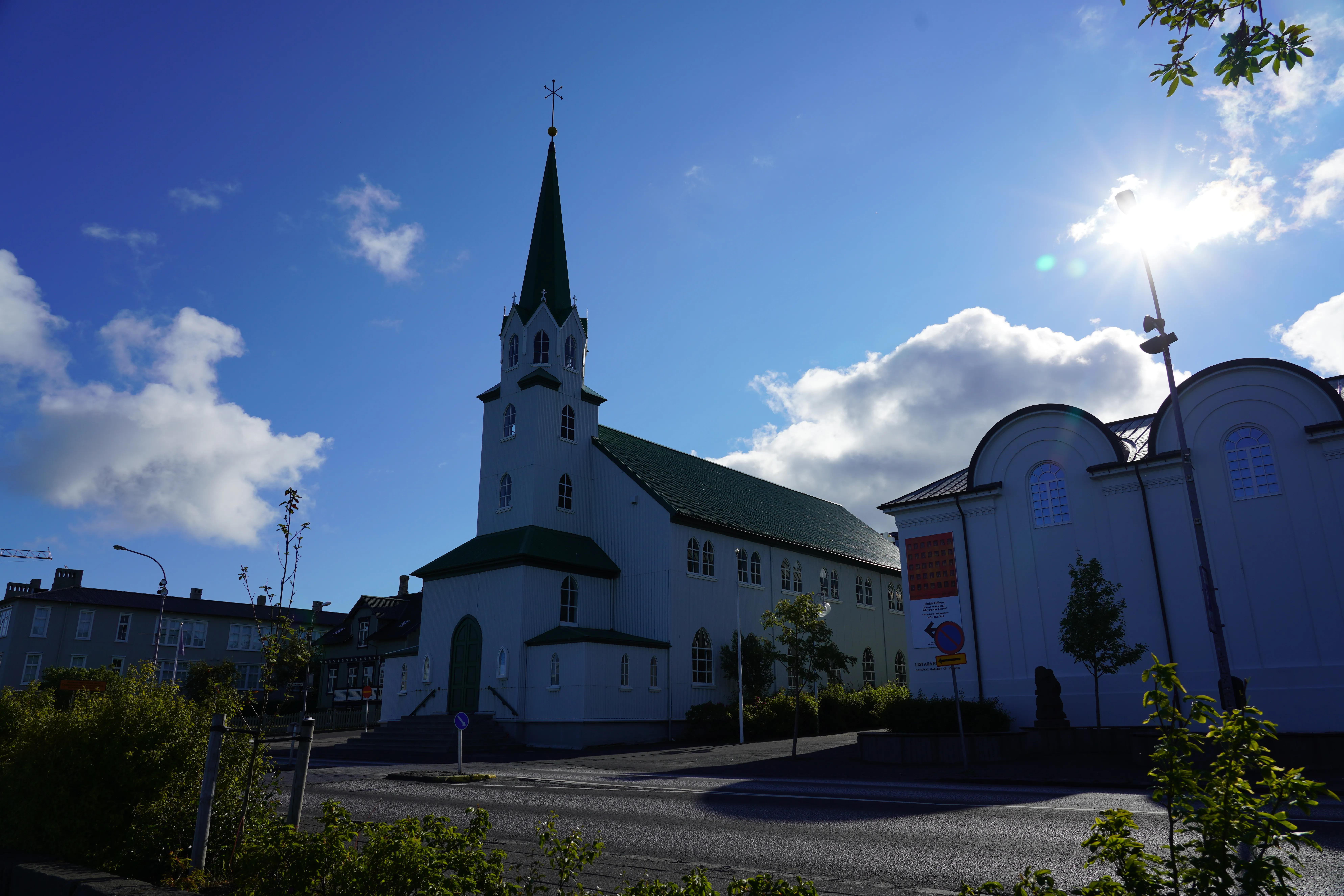 Iglesia blanca con una alta aguja verde y tejado verde sobre un cielo azul brillante con nubes, Fríkirkjan í Reykjavík