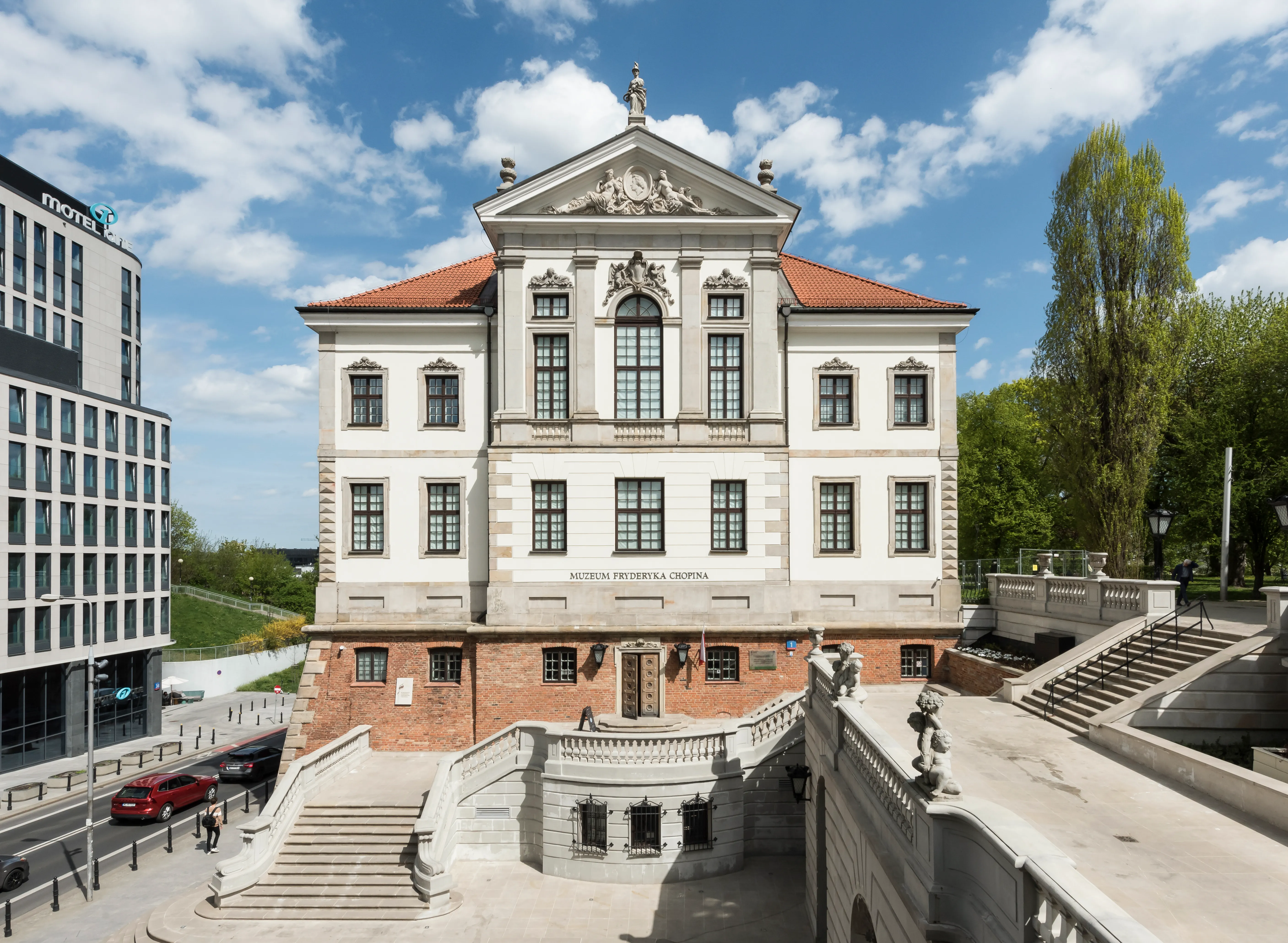 Classical building with a red-tiled roof and stone staircase under a blue sky