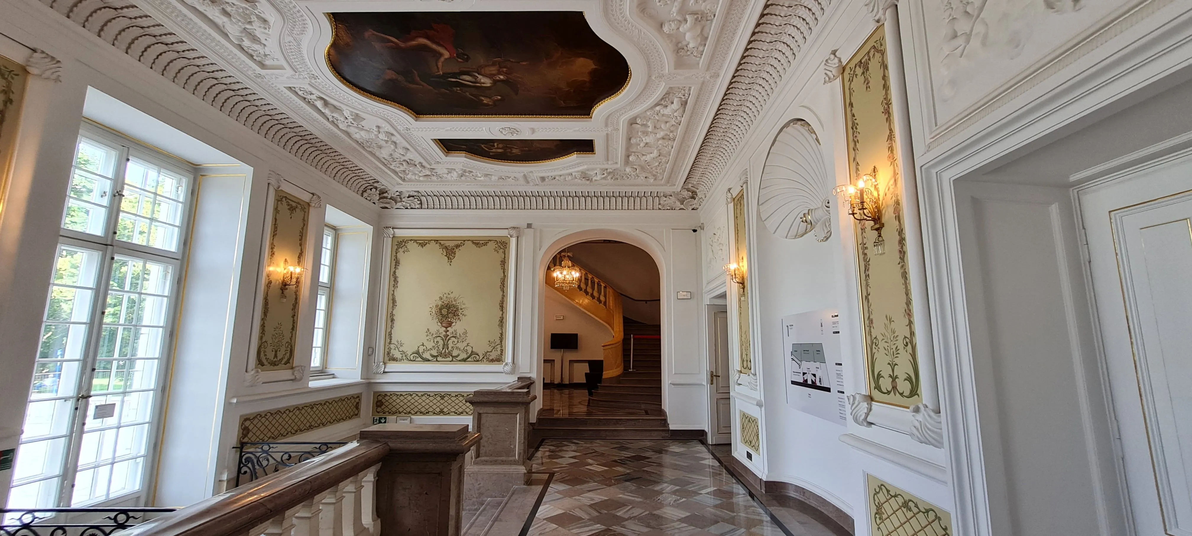 Ornate hallway with white stucco ceilings, gilded wall panels, and a marble floor in the Fryderyk Chopin Museum