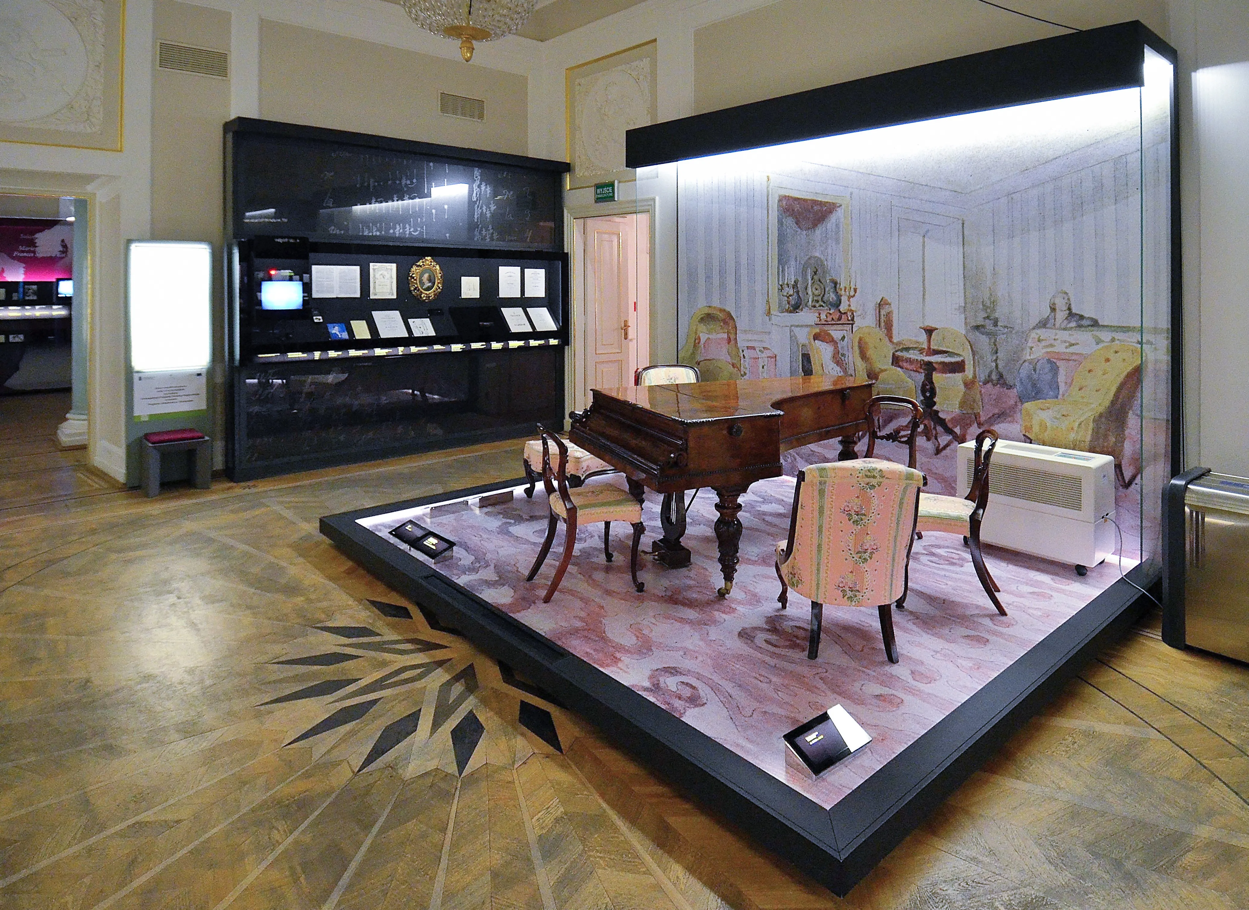Exhibition display with a grand piano, chairs, and a recreated room scene in a museum gallery
