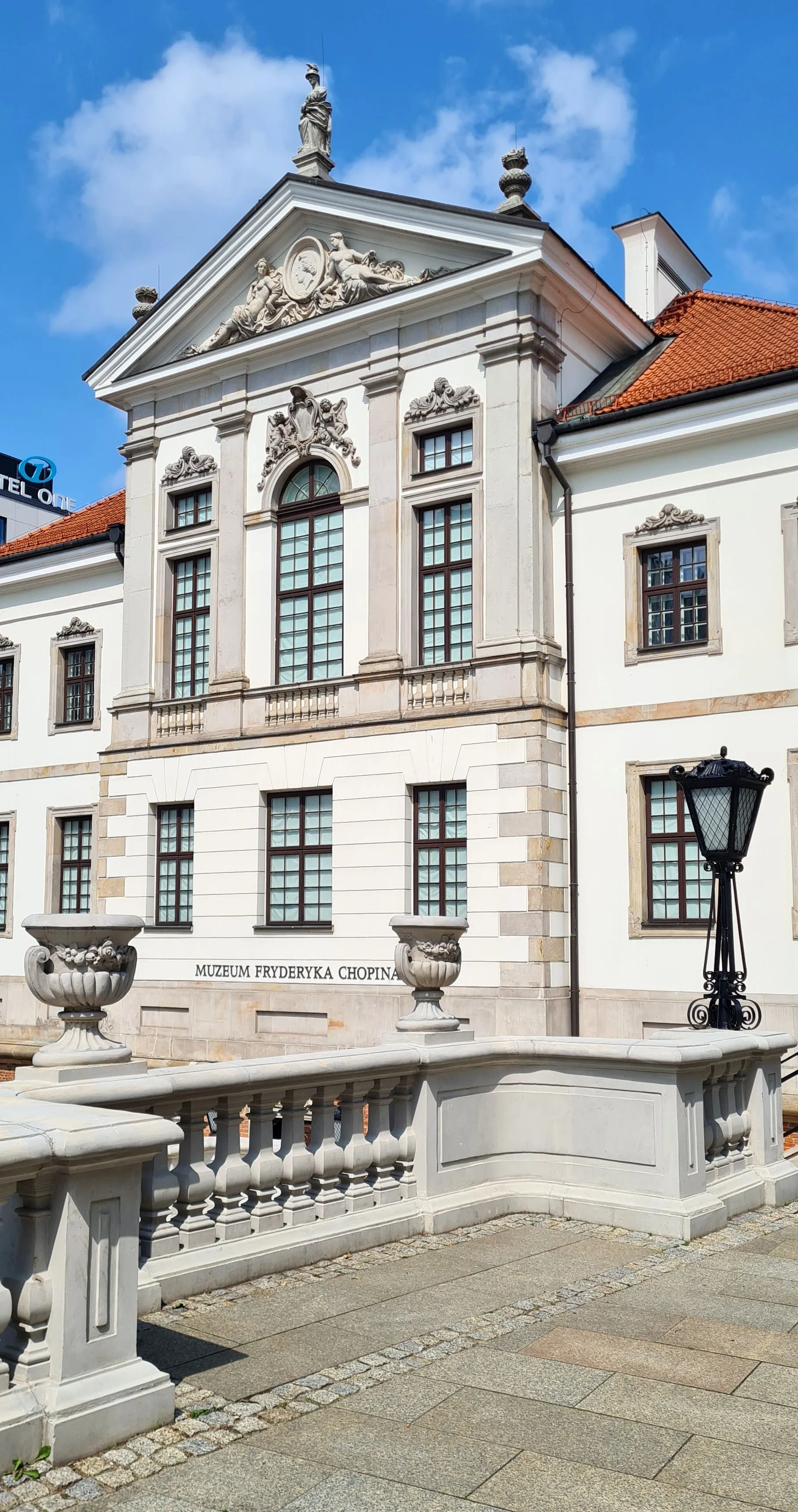 The Fryderyk Chopin Museum building with white stone facade, arched windows, and a sign reading 'MUZEUM FRYDERYKA CHOPINA' under a clear blue sky.