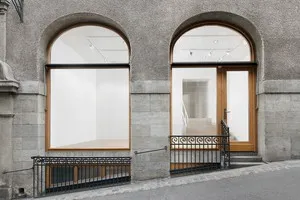 Fachada de piedra de un edificio que presenta dos grandes ventanas arqueadas con marcos de madera y una pequeña barandilla de metal negro a lo largo de la acera.