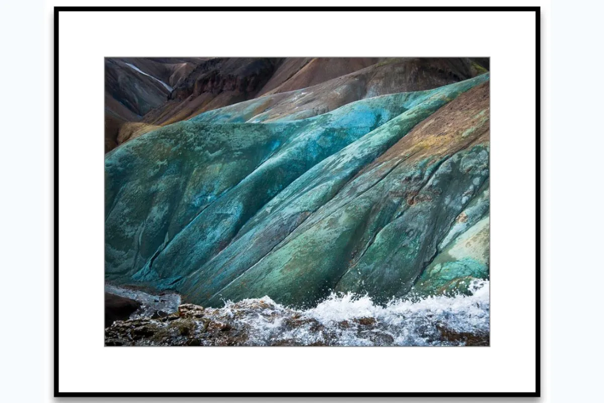 Fotografía enmarcada de formaciones rocosas ricas en minerales de tonos azul verdoso con agua blanca impetuosa en la base