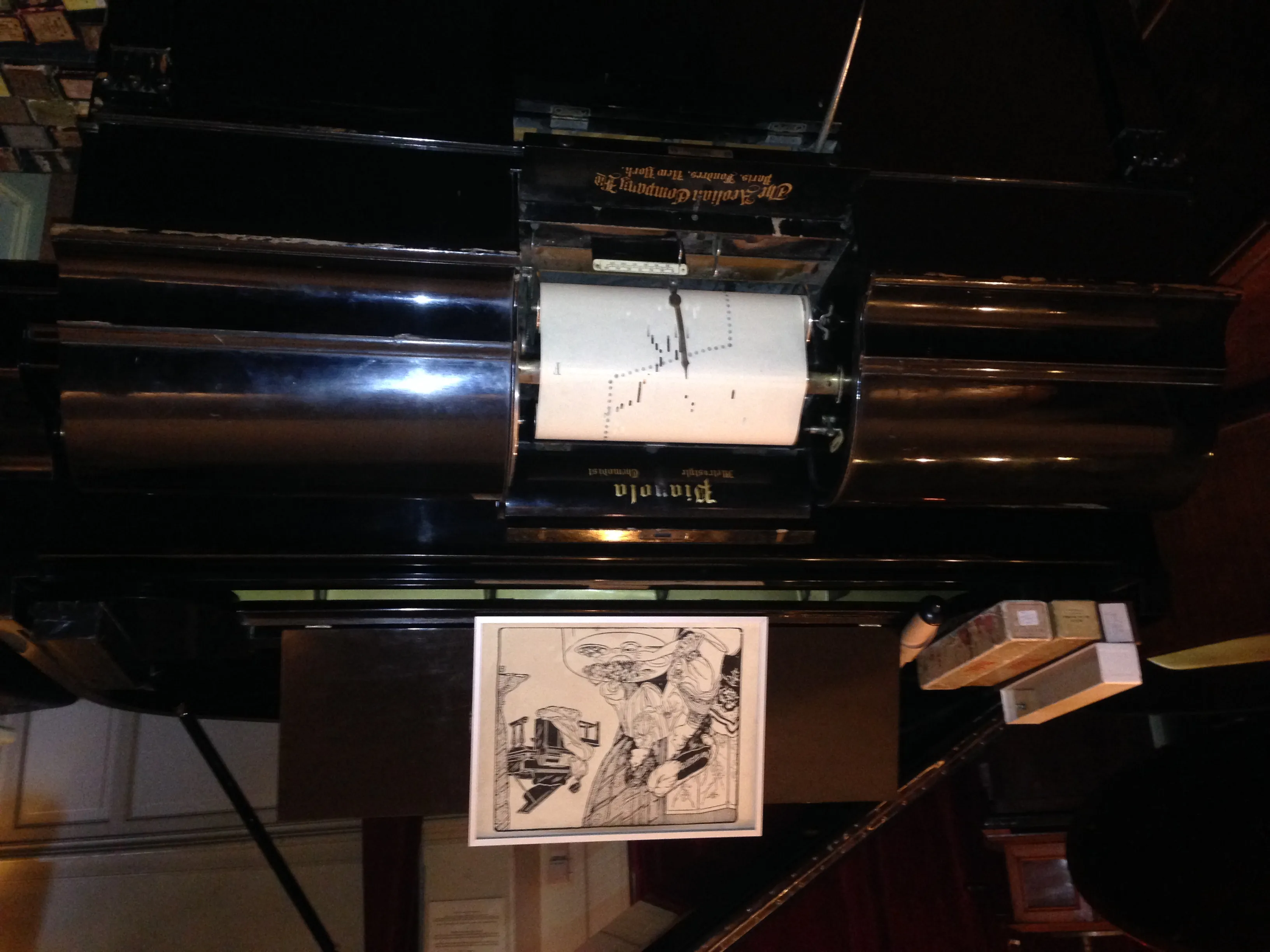 Close-up of a pianola mechanism with a paper roll and a framed illustration below