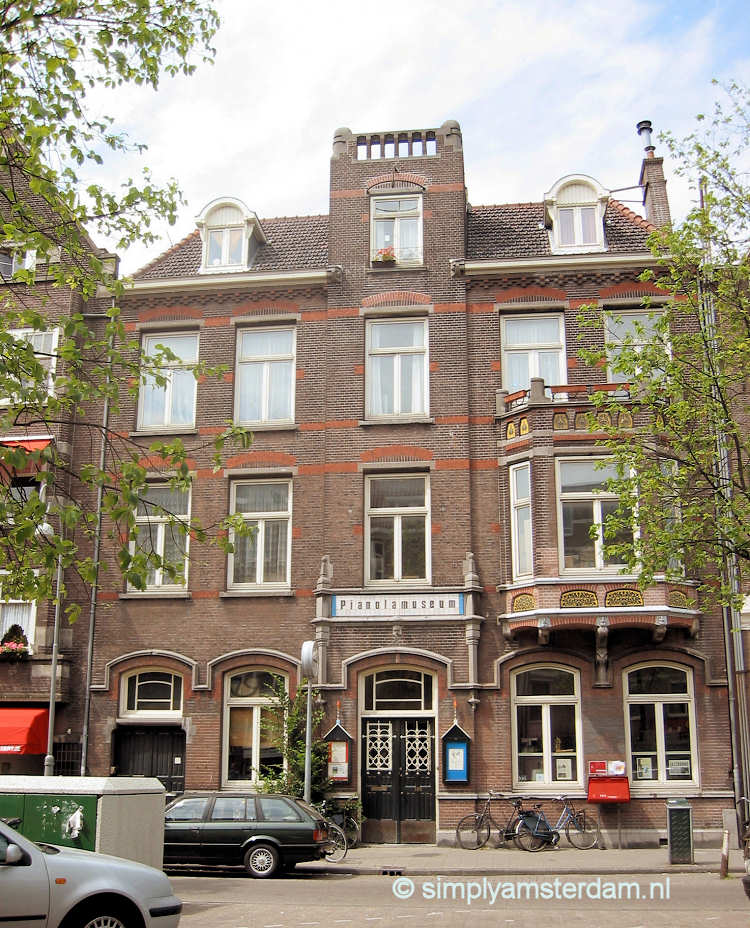 Historic brick building with 'PIANOLA MUSEUM' sign above entrance, street view with bicycles and parked cars