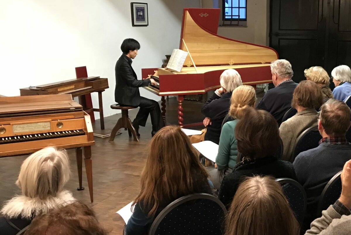 A performer plays a red and gold pianola for an audience in a room with historic keyboard instruments