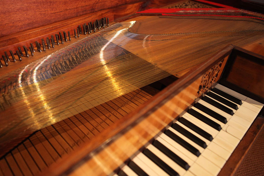 Close-up of a wooden pianola showing black and white keys, internal hammers, and strings in a well-lit setting.